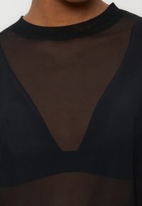 Άτομο που φοράει μαύρο διάφανο τοπ με τριγωνική αδιαφανή επιφάνεια που καλύπτει το στήθος και στρογγυλή λαιμόκοψη.