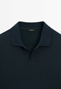 Polo bleu marine foncé à manches courtes, tissu texturé et col plat, avec l'étiquette du cou visible.