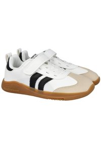Zapatillas blancas con rayas negras, punta de color beige y suela de goma texturizada. Cuenta con una correa de Velcro y cierre de cordones. Material sintético suave.