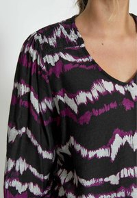 Blusa nera con motivo a zigzag in viola e bianco, con scollo a V e tessuto arricciato sulle spalle per un tocco di texture.