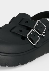 Sabot Crocs noir avec deux sangles réglables comportant des boucles argentées et une semelle épaisse et texturée.