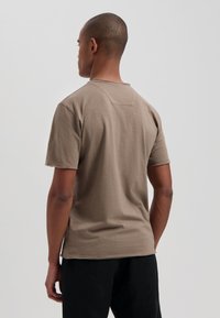 Half-sleeve, ronde hals t-shirt in beige stof. Ontspanning fit met zijsplitsingen, zichtbare stikdetails op de rug en een gladde textuur.