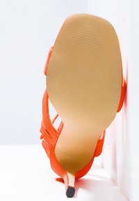 Chaussure à talon haut orange avec un extérieur lisse, un design ouvert à l'arrière, une pointe effilée et une semelle striée. Le talon est fin et élancé, avec une forme conique.