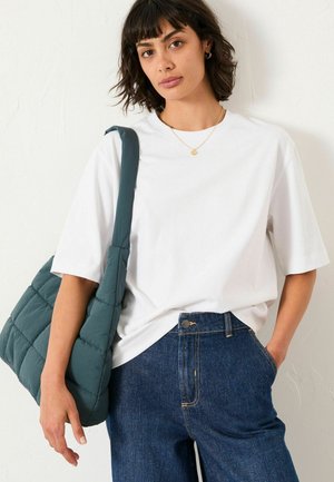 White short-sleeve t-shirt paired with high-waisted dark blue denim jeans. A textured, teal quilted shoulder bag is slung over the shoulder.