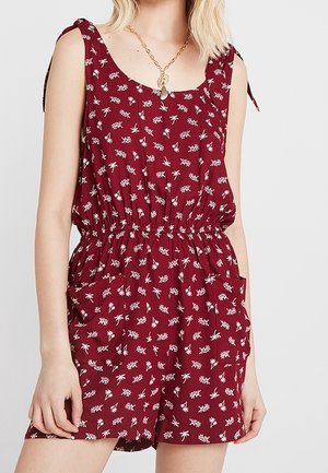 Combinaison short florale bordeaux avec bretelles fines, taille élastique et poches ; motifs de petites feuilles blanches partout. Tissu léger.