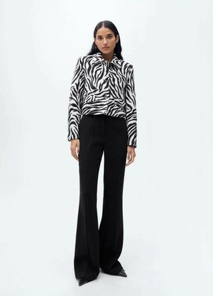 Sort og hvid zebra-stribet cropped jakke med krave, parret med højtaljede sorte slacks og spidse sorte sko.