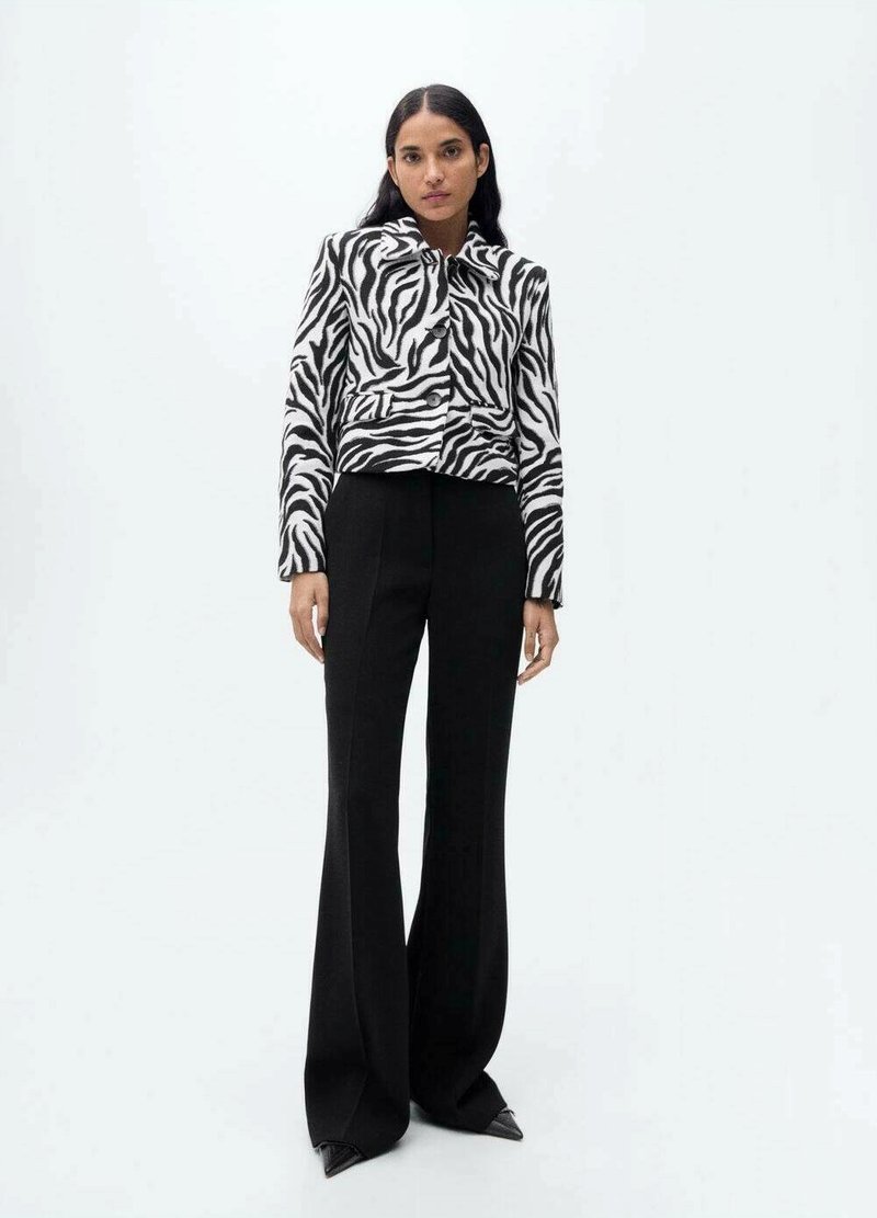 Zwart-wit gestreepte cropped jacket met een kraag, gecombineerd met hoge zwarte flairbroek en scherpe zwarte schoenen.