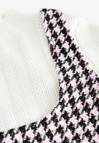 Melnā, baltā un rozā houndstooth raksta auduma siksna, kas apvienota ar teksturētu balto adījumu. Siksnai ir pūkaina tekstūra un šūtu detaļu aksesuārs.