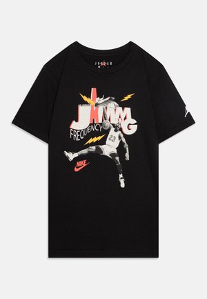 Sort t-shirt med grafik af basketballspiller, der dunker, teksten "Jamming Frequency", gule lyn og rød Nike-logo.