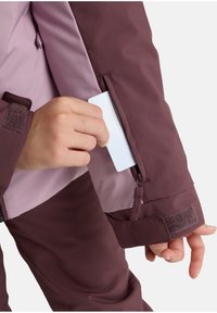 Bordeaux jack met een paarse voering, met een zijzak voor kaarten, verstelbare manchetten met klittenband en een gladde, waterafstotende textuur.