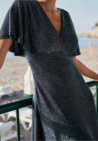 Iskrivé černé šaty s volánkovými rukávy, výstřihem do V, přiléhavým živůtkem a měkkou, texturovanou látkou. Vhodné na pláž nebo neformální příležitosti.
