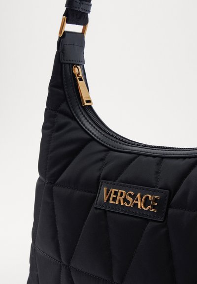 Geantă de umăr neagră, matlasată, cu logo-ul auriu Versace, finisaj neted, accente din piele și un fermoar cu o agatatoare aurie.