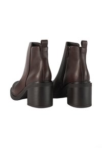 Stivaletti in pelle marrone, con punta arrotondata, chiusura zip e tacco spesso a coste neri. Texture liscia con dettagli minimi.