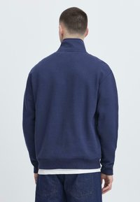 Felpa blu navy con colletto alto, polsini e orlo a costine. Realizzata in tessuto morbido, presenta un design semplice e pulito, privo di fantasia.