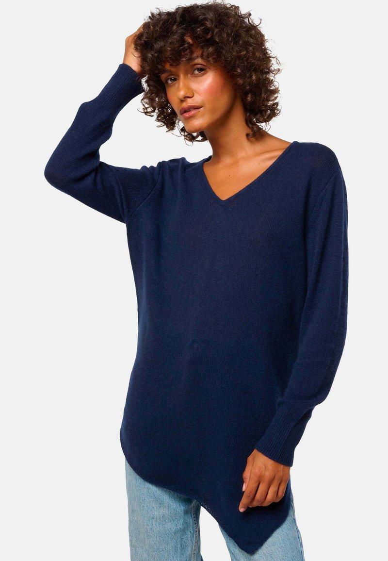Marineblaues gestricktes Sweatshirt mit V-Ausschnitt, langen Ärmeln und asymmetrischem Saum. Strukturierter Stoff mit legerem Sitz. Kombiniert mit hellblauen Jeans.