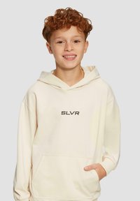 Krémová mikina s kapucňou a prednou vreckom, s textom "SLVR" v tmavom písme na hrudi. Mäkkučký, voľný materiál.