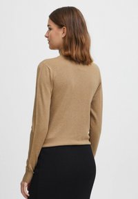 Maglione attillato color marrone chiaro realizzato in materiale morbido. Presenta maniche lunghe e un design semplice, abbinato a una gonna nera a costine.