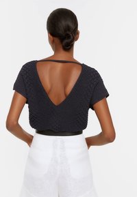 Navy gestructureerde top met een V-hals aan de achterkant, korte mouwen en een losse fit, gecombineerd met witte hoge taille shorts, voorzien van twee achterzakken.