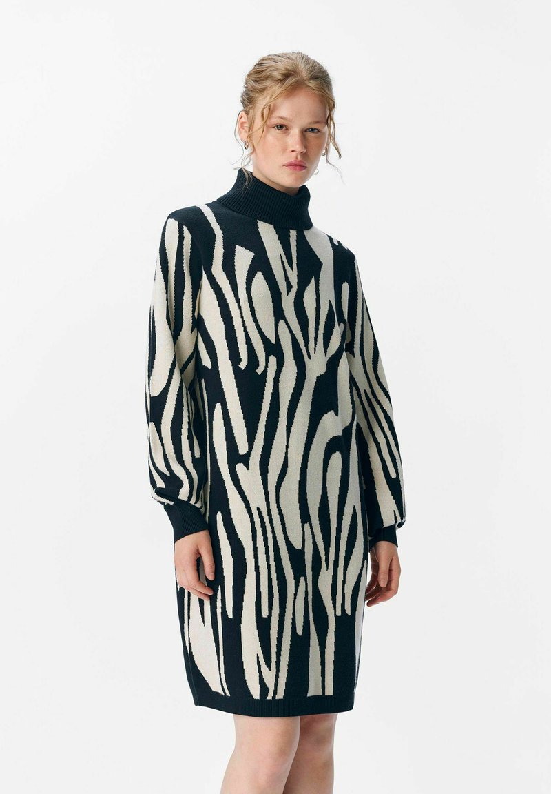 Robe en tricot avec un col haut, présentant un motif abstrait audacieux noir et crème, des manches longues et une coupe décontractée.