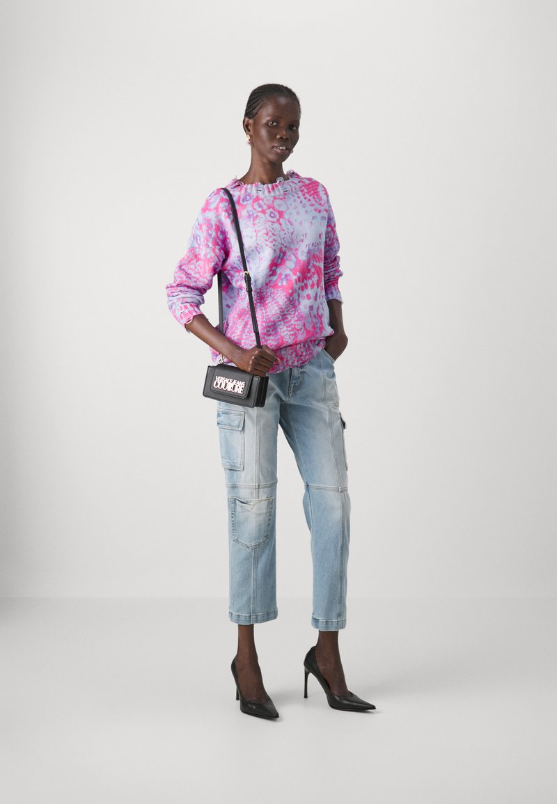 Roze en paarse tie-dye sweatshirt met een gerimpelde halslijn, gecombineerd met lichte cargobroeken en zwarte puntige hakken. Kleine zwarte handtas.