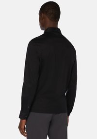 Czarna koszula z długim rękawem i kołnierzykiem, gładka w dotyku, z zapięciem na guziki przy mankietach i dopasowanym kroju, widoczna z tyłu.