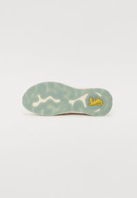 Semelle de chaussure avec un motif ondulé en bleu clair et crème, ornée d'un petit logo jaune. Fabriquée en caoutchouc, elle présente une adhérence texturée et de la flexibilité.