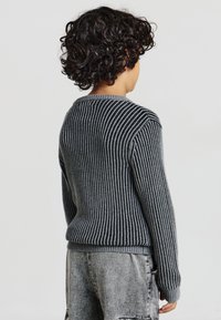 Maglione grigio a righe con texture a coste, scollo rotondo e maniche lunghe, abbinato a pantaloni corti di jeans grigi.