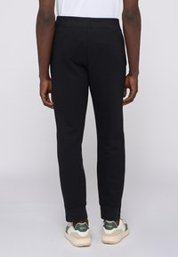 Svarta sweatsshorts med en åtsittande design, ribbade muddarna och resårmidja. Slät textur; bärs med vita och gröna sneakers.