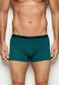 Boxer in cotone verde con elastico blu navy in vita, sul quale è stampato il marchio "yamamay" con lettere scure. Texture liscia, design aderente.