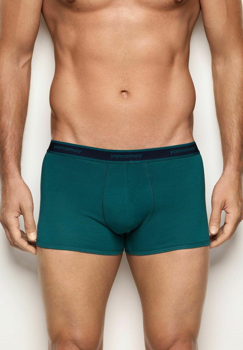 Boxer in cotone verde con elastico blu navy in vita, sul quale è stampato il marchio "yamamay" con lettere scure. Texture liscia, design aderente.