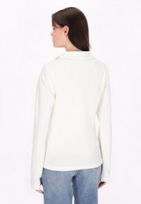 Hvid langærmet top i blødt stof med en afslappet pasform og krave, parret med lyseblå jeans med klassisk snit.