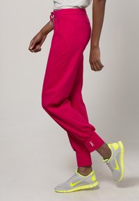 Roze joggingbroek met elastische manchetten, twee zijzakken en een taille met trekkoord, gecombineerd met grijze sneakers met neongele accenten.