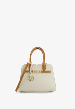 Crèmekleurige handtas met bruine handvatten, verstelbare schouderriem, gouden sluiting en ronde gouden hanger tegen een witte achtergrond.