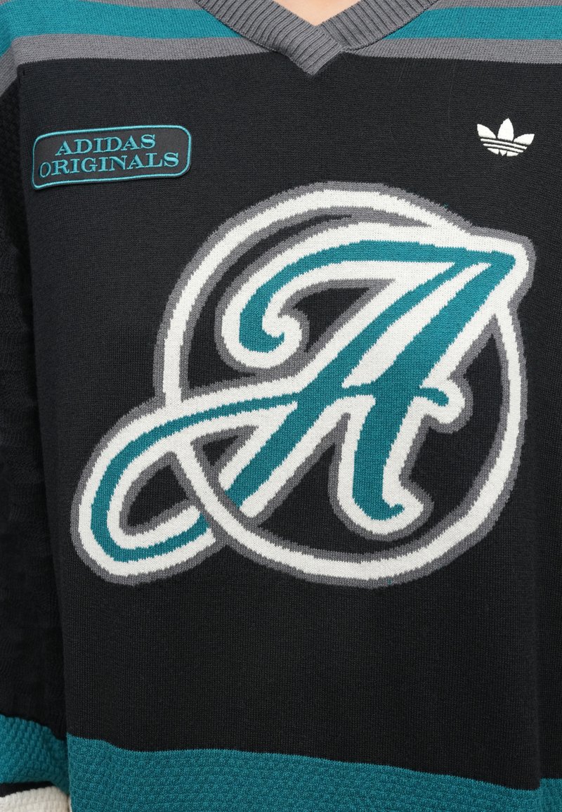 Maillot en maille noire avec des accents turquoise, gris et blanc. Présente un grand logo stylisé en forme de "A" et une étiquette "Adidas Originals". Conception à encolure en V.