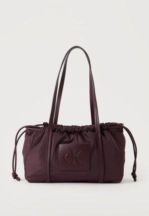 Σκούρο μωβ τσάντα Calvin Klein με μακριά λουριά, σούρες στο πάνω μέρος, πλαϊνά κορδόνια και ανάγλυφο λογότυπο μπροστά.