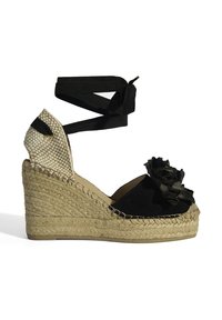 Schwarze Wedge-Espadrille mit gewebten beige Akzenten. Verfügt über eine dekorative Blüte an der Zehe und schwarze Riemen. Schnurähnliche Sohle.