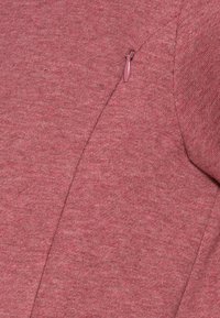 Un pull en tissu texturé et chiné de couleur rose chaud, présentant un petit détail de fermeture éclair sur la couture de l'épaule gauche.