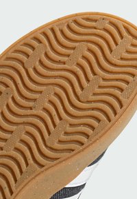 Rubber shoe outsole with a wavy tread pattern, featuring a tan color with flecks, and a textured surface for grip and durability.
