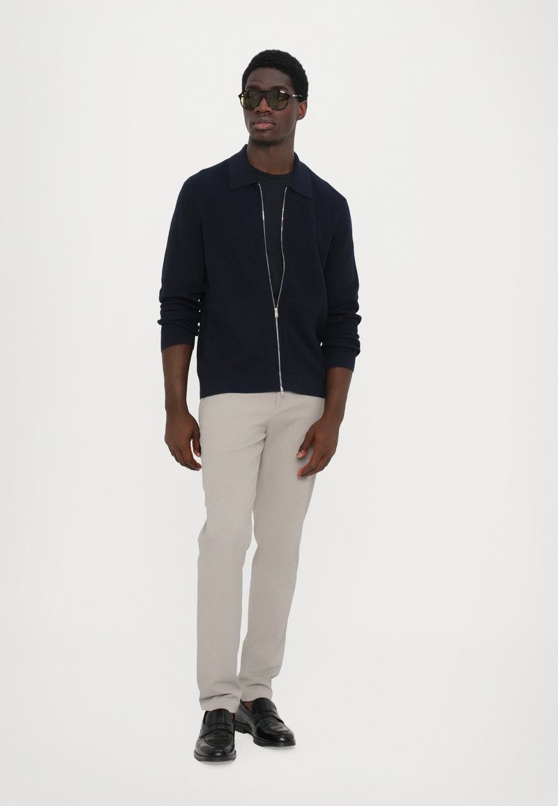 Marineblå zip-op strikketrøje med krave, parret med lysegrå bukser og sorte læder mokkasiner. Slim fit, glat tekstur.