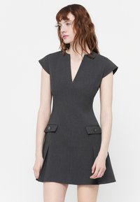 Siva uska haljina s dubokim V-izrezom, kratkim kap sleeves i bočnim džepovima s detaljima tipki. Napravljena od teksturirane tkanine.