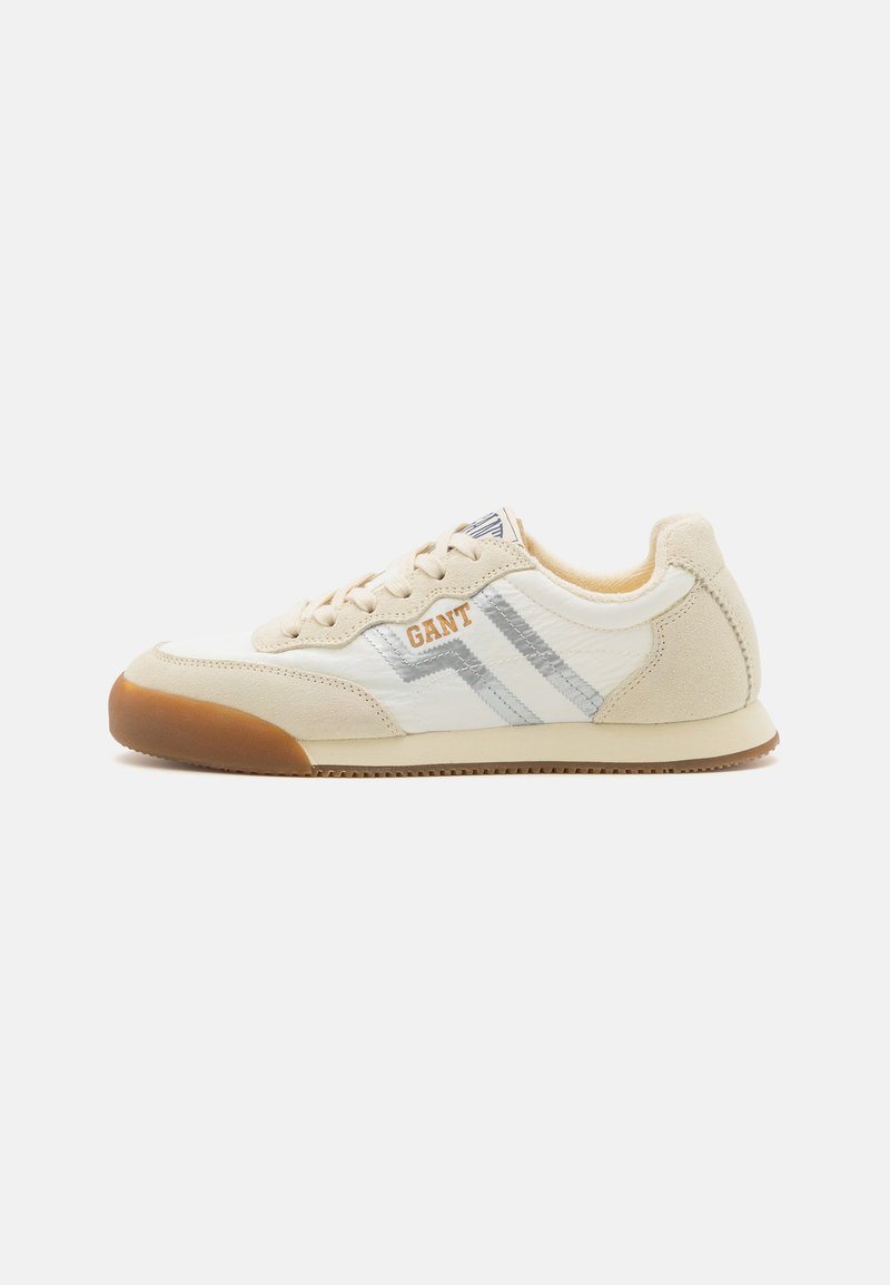 Scarpa sportiva beige con tomaia in suede e materiale sintetico, caratterizzata da tre strisce argentate e un logo arancione. Suola in gomma con grip testurizzato.