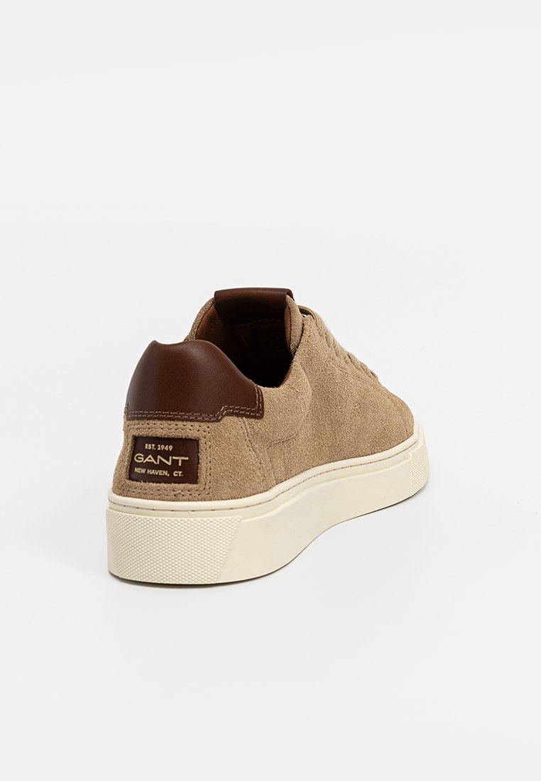 Sneaker in suede beige con un cappuccio del tallone in pelle marrone, suola in gomma bianca e un'etichetta con logo GANT sul retro. Design classico a basso profilo.
