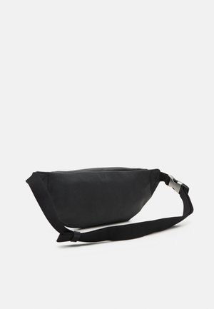 Sac banane en cuir noir avec sangle réglable et boucle argentée sur un fond clair uni.