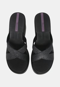 Sandali neri con incroci sulle cinghie, caratterizzati da una texture glitterata. Suola piatta con una linea di accentuazione viola, contrassegnata con "Ipanema."