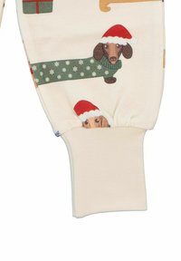 Krämfärgad tyg med festliga dachshundtryck i tomteluvor, med en ribbad mudd. Designen innehåller gröna accenter och julmotiver.