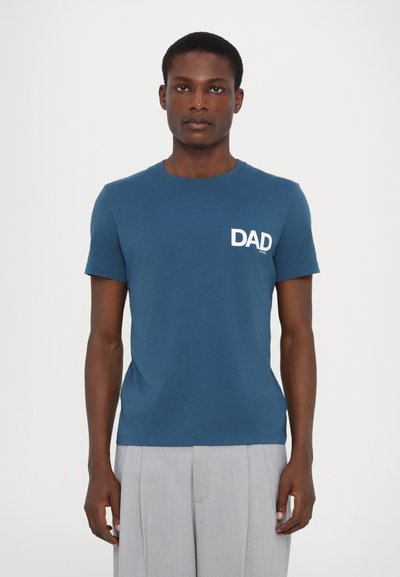 Türkises Baumwoll-T-Shirt mit kurzen Ärmeln, ausgestattet mit einem weißen "DAD"-Druck auf der linken Brust. Gerade Passform, glatte Textur.