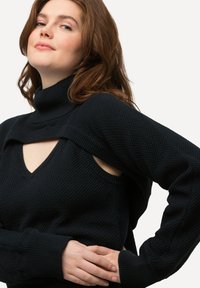Schwarzer Strickpullover mit hohem Kragen und Ausschnitten an den Schultern. Strukturiertes Muster und gerippte Bündchen. V-Ausschnitt-Details.