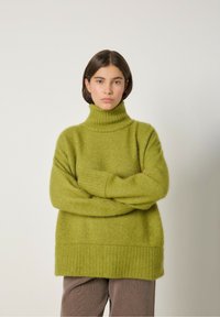 Läikiv roheline, ülisuur soe kampsun kõrge ribaga kaelusega, ribaga alläärega ja pikkade varrukatega. Pehme, tekstureeritud kangas.