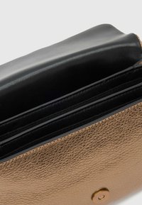 Bronsefarget lærpung med teksturert finish, som har en svart innside og flere kortlommer, sikret med en rund knappelukking.