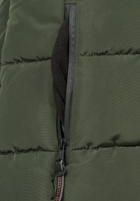 Green puffer jacket section with a zipper and a fleece-lined pocket. Features tonal stitching and a branded zipper pull for detail.